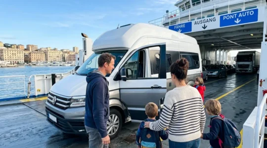 Eine Familie begleitet ihr Wohnmobil beim Einfahren auf das Fahrzeugdeck einer modernen Fähre im Mittelmeerhafen, morgendliches Sonnenlicht, Alltagsszene ohne Posing